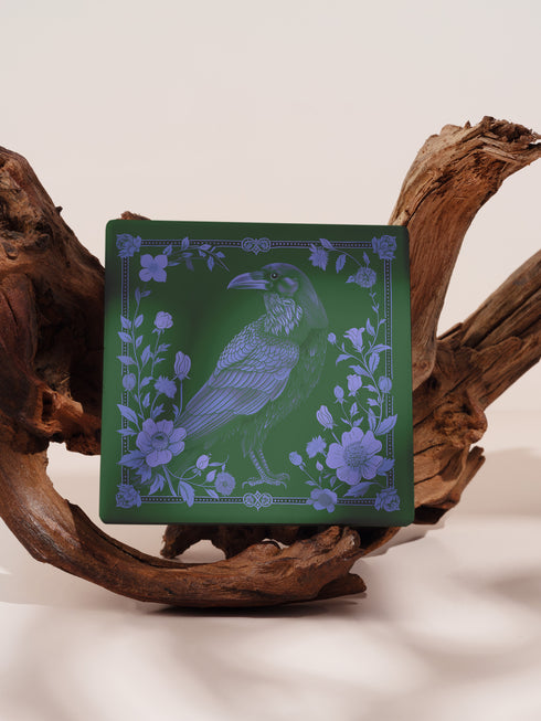 Square ceramic coaster featuring intricate lavender illustration of a raven surrounded by botanical elements on forest green background, with ornate border design and cork backing.